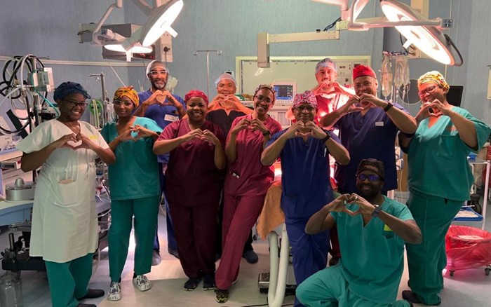 Nine health professionals posing for a photo in a theatre room.