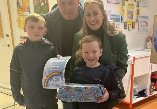 Two parents and children smile with a certificate and a gift