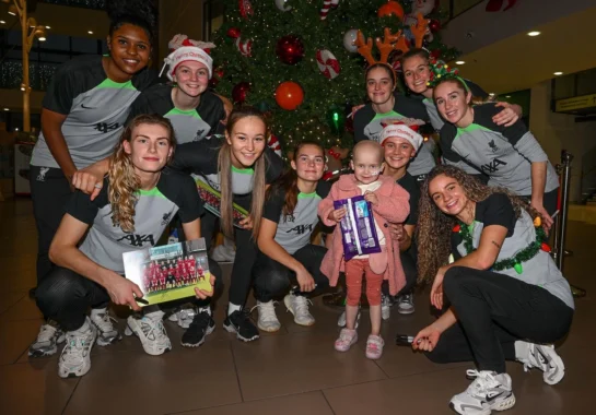 Picture of a little girl holding Christmas selection boxes with players from LFC Women's first team.