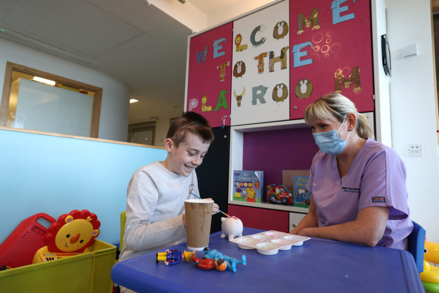 A child painting sat next to a play specialist at Alder Hey Children's Hospital